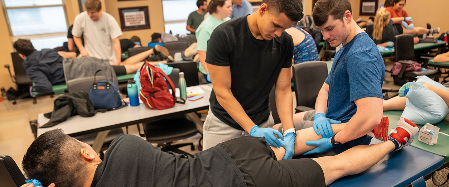 Two students practicing dry needling with a third in a PT lab
