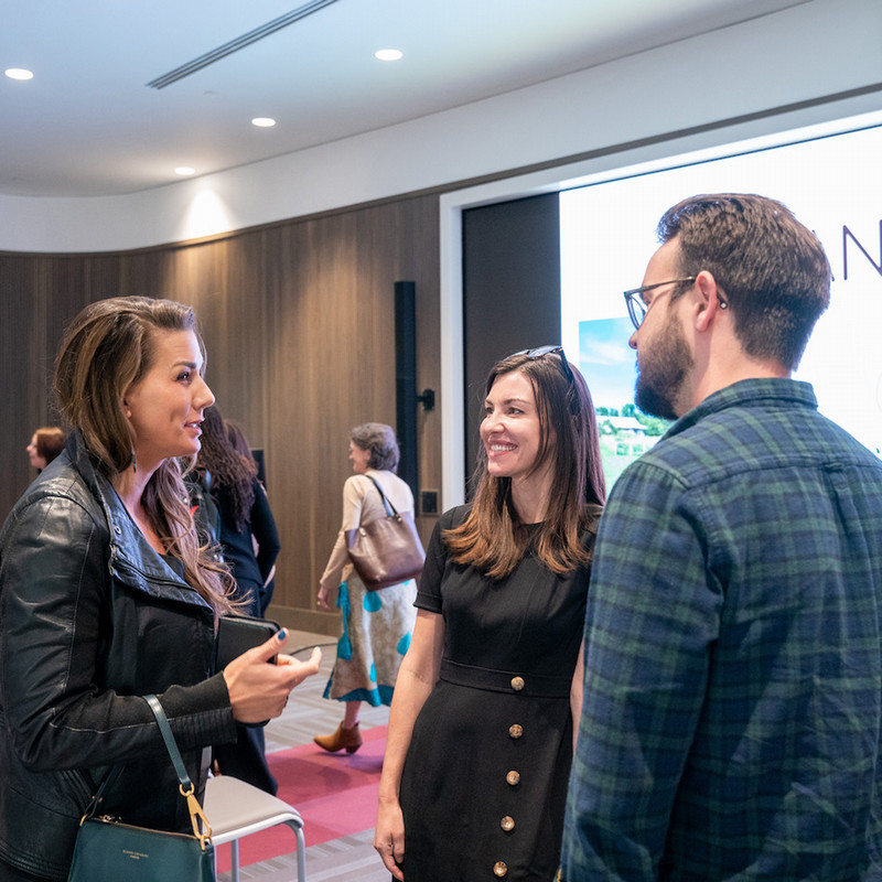An indoor photo of a small group of a man and two women engaged in conversation