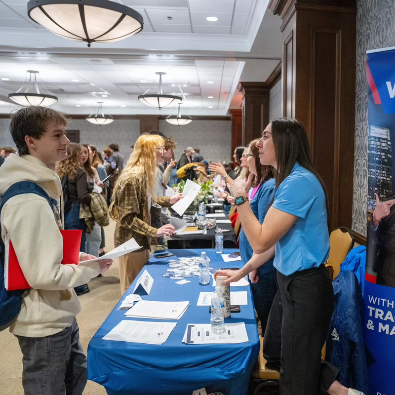 Students interact with recruiters at a career fair, with one student speaking to a representative at the WSMV 4 News table. A banner beside the booth displays anchors Tracy Kornet and Marius Payton with the text “WSMV 4 News at 10.” The event takes place in a large, well-lit conference room filled with booths and attendees.