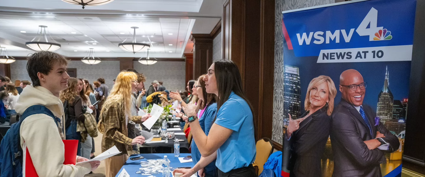 Students interact with recruiters at a career fair, with one student speaking to a representative at the WSMV 4 News table. A banner beside the booth displays anchors Tracy Kornet and Marius Payton with the text WSMV 4 News at 10. The event takes place in a large, well-lit conference room filled with booths and attendees.