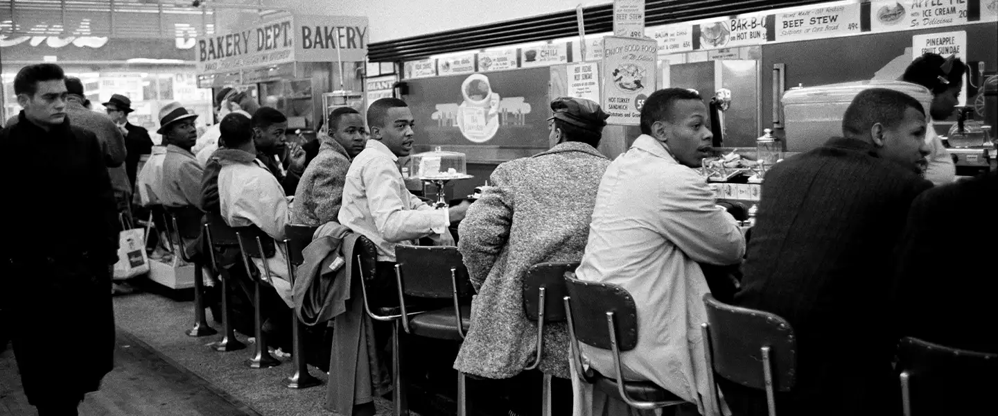 An indoor photo of men sitting at a soda fountain at McLellans in 1960